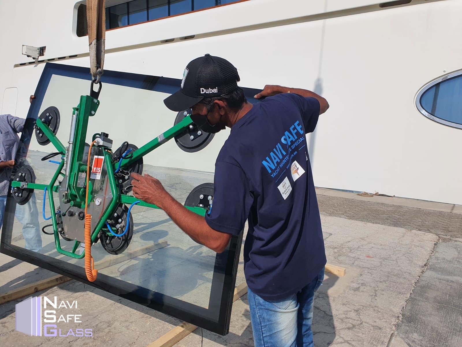 Worker uses a green vacuum lifter to move a large glass pane for a yacht.